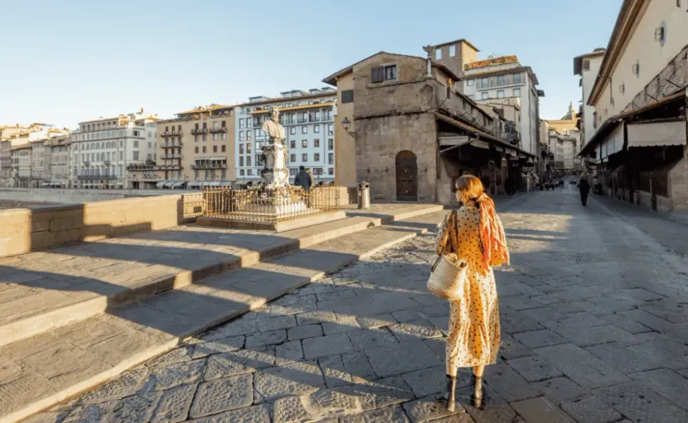 Woman with colorful shawl and sunglasses walking on famous old bridge, called Ponte Vecchio, in Florence. Concept of traveling italian landmarks.